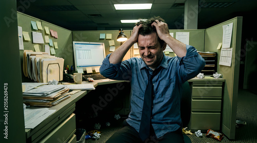 Stressed office worker pulling hair in frustration at a cluttered desk with paperwork