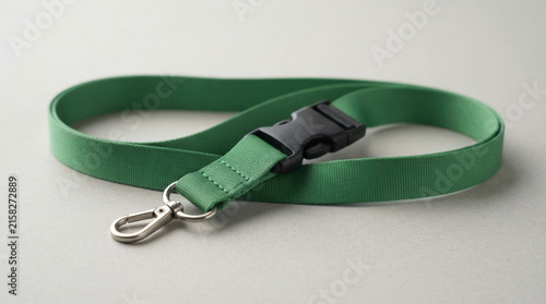 Green woven fabric neck lanyard with black plastic safety breakaway buckle and silver metal swivel lobster claw hook on gray background.