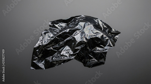 Single piece of crushed black plastic foil texture creating abstract irregular shadows and highlights against neutral monochromatic gray background.