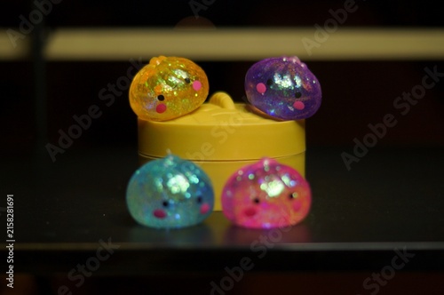 фотографія Four colorful glitter-filled sensory toys are arranged around a round yellow container on a dark tabletop