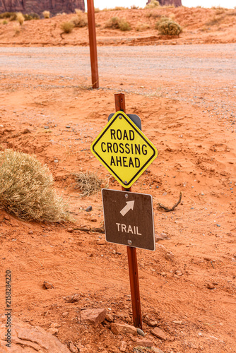 Yellow Road Crossing Ahead sign and brown trail marker at Monument Valley. 