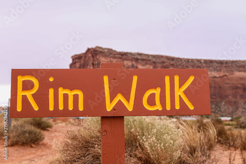 Rim Walk wooden trail sign with red rock mesa background in Monument Valley.