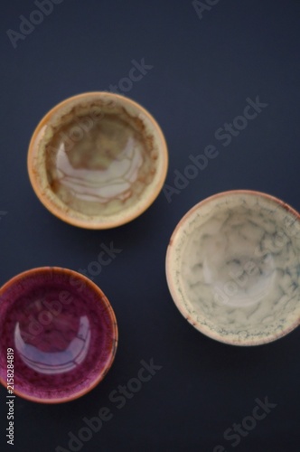 Three handcrafted ceramic bowls in beige, cream, and burgundy are arranged in an overhead composition on a dark background. The image represents visual balance, creative craftsmanship, individuality