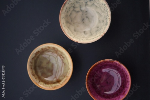 Three handcrafted ceramic bowls in cream, beige, and burgundy form a triangular overhead arrangement on a dark background. The image represents visual balance, creative composition, and individuality