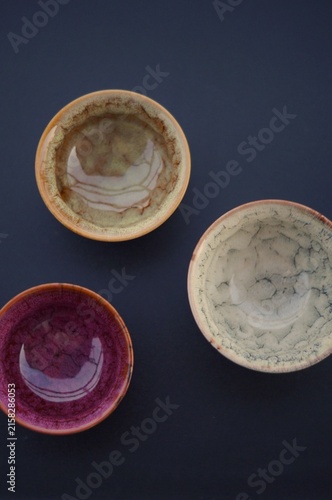 Three colorful handcrafted ceramic bowls form a balanced overhead arrangement on a dark background. The image represents creative composition, artisanal craftsmanship, visual harmony, and the