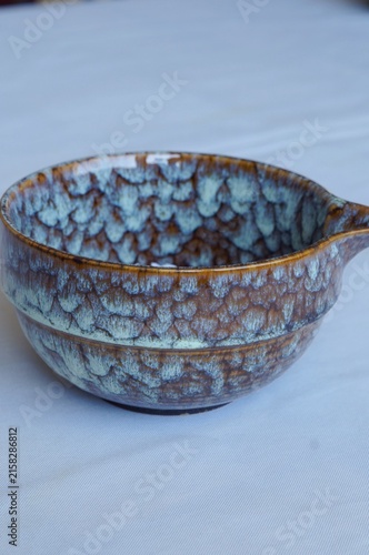 Handcrafted ceramic bowl with blue and brown glaze rests on a white surface. The image represents artisan craftsmanship, simplicity, authenticity, and timeless tableware design.