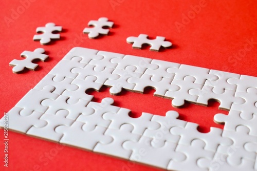 Photography High angle perspective of an incomplete white jigsaw puzzle showing a rectangular gap over a solid red textured background