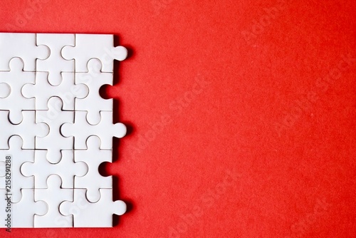 Fotografie A section of an incomplete white jigsaw puzzle assembled on the left side against a bright red background