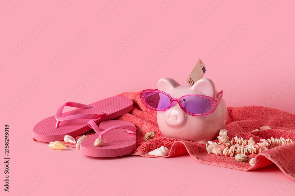 Fototapeta premium Pink piggy bank with sunglasses and euro banknote, summer vacation savings with flip-flops and seashells
