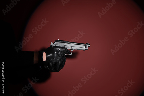 Canvastavla Hand in black leather glove holding a silver pistol against a dark red backgroun