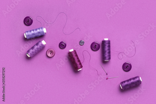 Obraz na plátne Spools of thread with ball pins and buttons on purple background