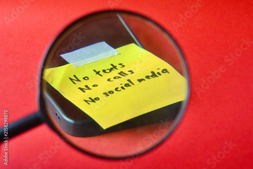 Foto A magnifying glass focuses on a yellow sticky note attached to a phone reading No texts, No calls, No social media over a stark red background