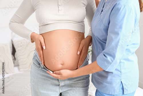 Young doula touching pregnant womans belly in bedroom, closeup