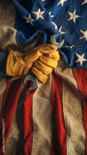 Worn work glove holding wrench on the American flag. Symbolic of hardworking blue collar workers, USA manufacturing, pride in products Made in United States of America, or to celebrate US Labor Day.