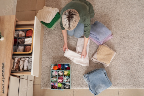Beautiful young woman organizing clothes at home, top view