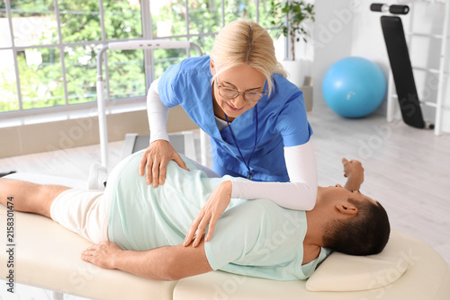 Female physiotherapist working with young man on couch in rehabilitation center