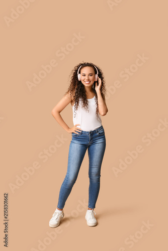 Happy young African-American woman in headphones on beige background