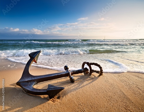 a classic ship anchor resting on a sandy beach with waves in the background