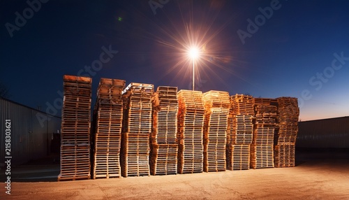 wooden pallet stack at night under industrial light creating warm and quiet atmosphere in outdoor storage area