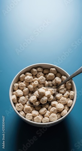 Bowl of cereal with milk and spoon on blue background.