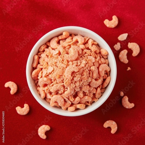 Bowl of crushed cashew nuts on red background.