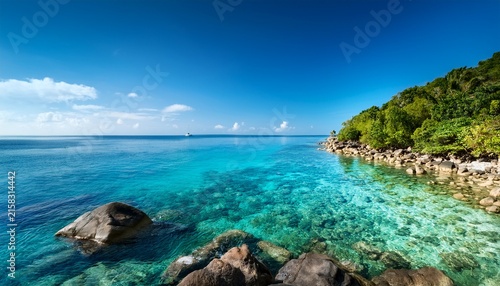 clear shallow sea laps against a rocky tropical shore with a lush green headland stretching into the calm ocean