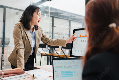 Asian Businesswoman Presenting Data Charts to Colleague on Computer Screen in Office