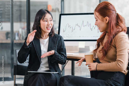 Two Asian businesswomen discussing financial data and stock chart in office