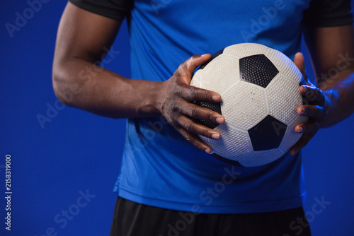 Mid-adult male holding white-black soccer ball at chest in studio wearing fitted blue shirt