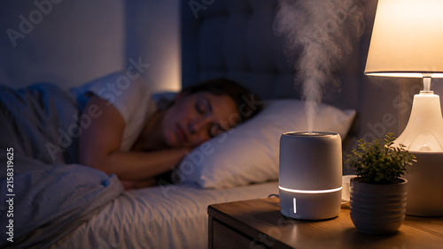 young woman sleeping peacefully in dark bedroom with air humidifier releasing steam vapor on nightstand next to bed for comfortable atmosphere and healthy sleep