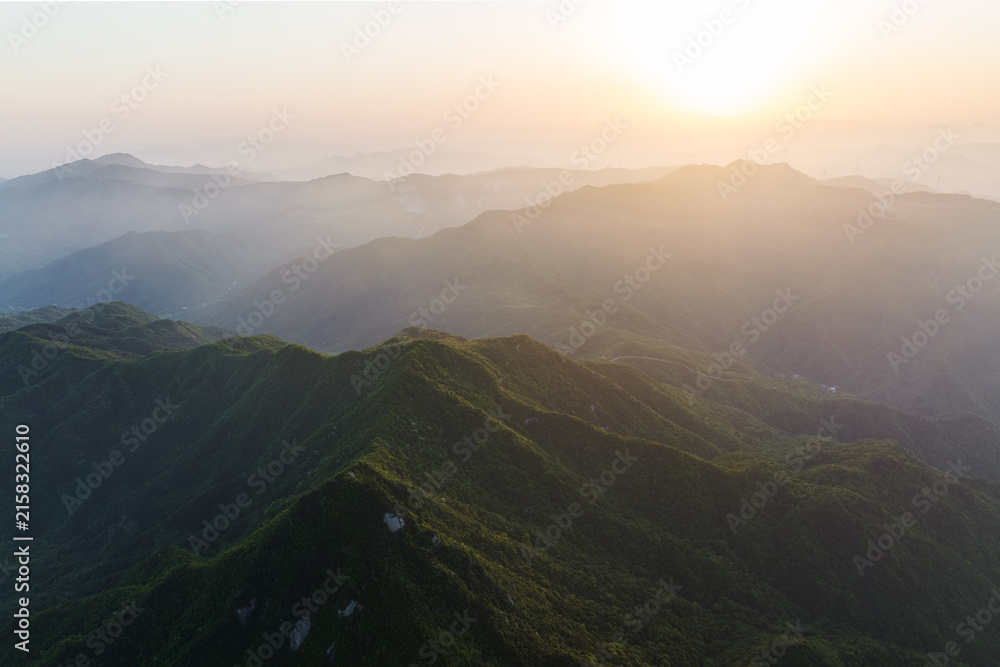 Fototapeta premium Layered mountain ranges at sunrise, with misty valleys and lush green slopes under warm morning light.