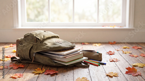 Canvas backpack with books, notebook and colored pencils spilling onto a wooden floor with autumn leaves is perfect for back-to-school social posts