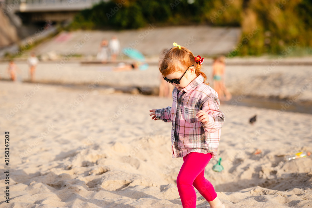 Fototapeta premium Child playing on the beach during sunset with sunglasses and a playful attitude
