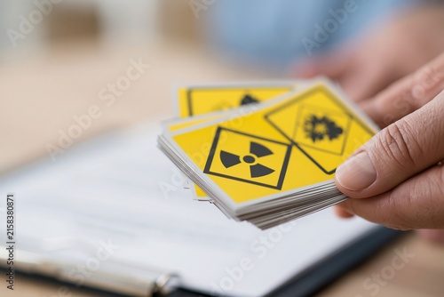 Close up of hands holding yellow hazard warning cards with radiation and toxicity symbols over documents.