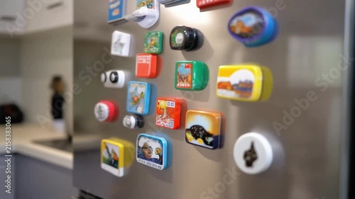 Close-up view of a stainless steel refrigerator door covered with colorful magnets of various shapes, sizes, and decorative designs