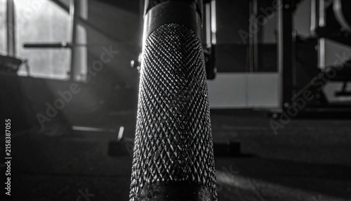 Close-up of textured knurled grip on a heavy weightlifting barbell in a dimly lit gym setting