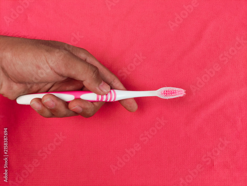Foto Close-up of a hand holding a pink and white toothbrush against a bright pink background, illustrating oral hygiene, dental care, tooth brushing, personal hygiene, and daily grooming