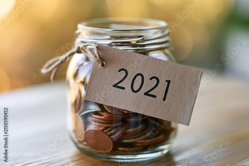 Glass jar filled with copper coins labeled 2021 representing savings and financial planning for the new year