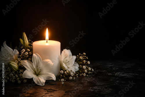 condolence background with burning candle and white lily flowers on dark background