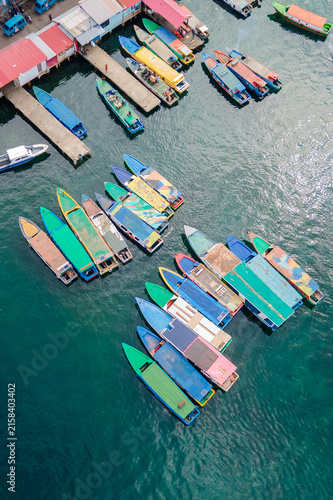 Top-down aerial view of colorful wooden passenger boats docked at Bitung port, Indonesia. These traditional vessels wait to ferry locals across the strait to Lembeh Island.