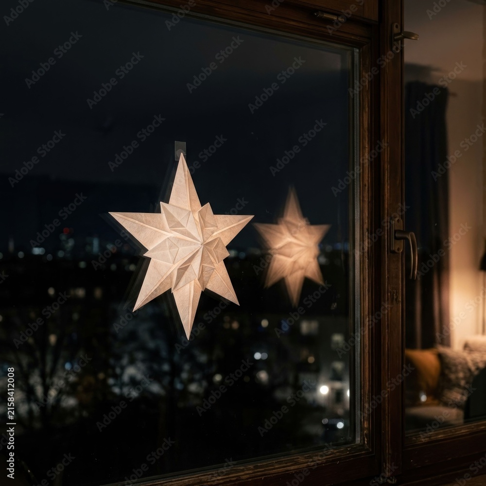 Obraz premium Illuminated Paper Stars Adorning a Window at Night with City Lights in Background.