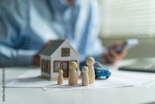 Obraz na płótnie Close-up of wooden family dolls with house model and toy car on insurance policy document at desk