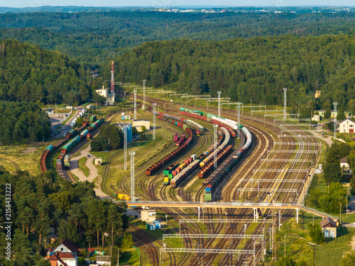 Aerial view of a large railway yard with multiple tracks and freight trains surrounded by dense green forest in Vilnius, Vilnius County, Lithuania.