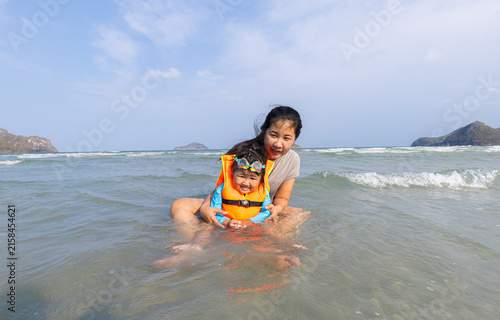 Foto Mother and Child Enjoying a Safe Day at the Beach,A mother sits in the shallow turquoise sea, tenderly holding her young child who is wearing a bright orange life vest and swim goggles