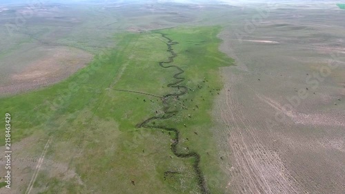 River cuts through barren hills in Turkmenistan, bringing green contrast to an arid valley.
