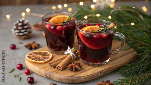 Two Glasses of Hot Mulled Wine with Cranberries, Orange Slices, and Cinnamon Sticks on Wooden Board with Festive Christmas Background