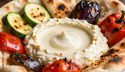 Harissa dip surrounded by roasted vegetables, creamy dip in the center with charred zucchini, roasted bell peppers, eggplant and toasted pita around it, extreme close-up composition