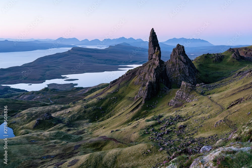 Naklejka premium The Iconic Rock Spire Rising Over Verdant Hills Beneath Distant Peaks