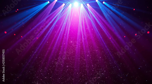 Stage lights beaming down on an empty venue with purple and blue hues and sparkling particles