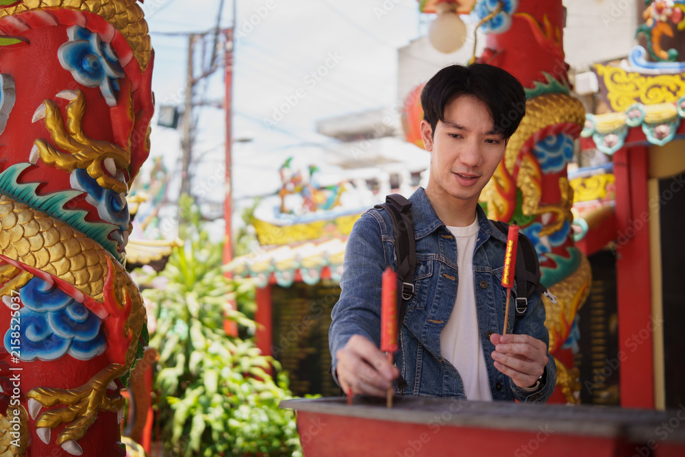 Obraz premium Young Asian tourist placing incense into a temple burner after prayer.